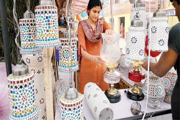 Woman examining handcrafted mosaic glass lamps at an Indian street handicrafts market stall