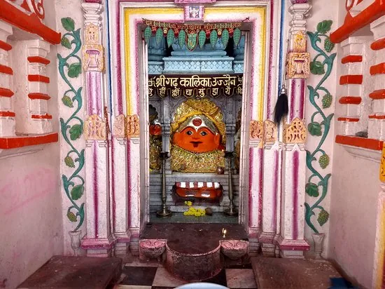 Interior view of Shri Gadikalika Temple in Ujjain, featuring a vibrant statue of Goddess Kali adorned with garlands and gold, framed by ornate pink and green architecture.