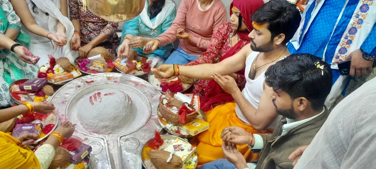 Devotees gathered around a Shiva Lingam during a vibrant Mangal Bhat Puja, offering prayers and placing colorful items and flowers, showcasing Hindu spiritual traditions.