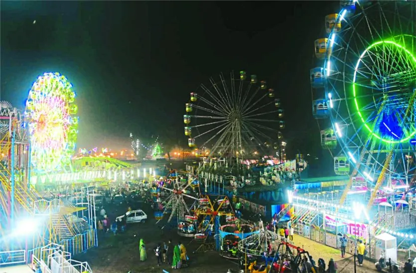 Vibrant night scene of Kartik Mela with multiple illuminated Ferris wheels, amusement rides, and lively crowd at Indian fairground